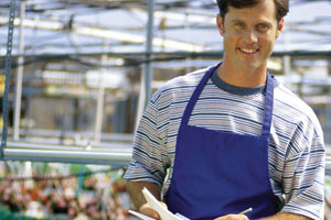 Retail greenhouse employee in blue apron holding clipboard